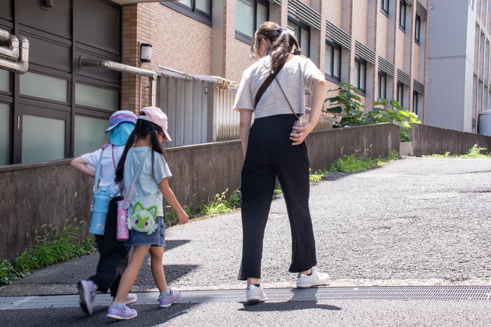 キャンパスの坂道を歩く子どもと大学生(後ろ姿)
