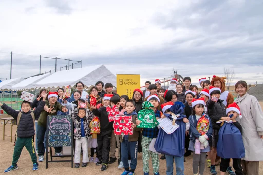サンタ帽をかぶった子どもたちと学生、社員有志が、テントの前で集合写真を撮っている