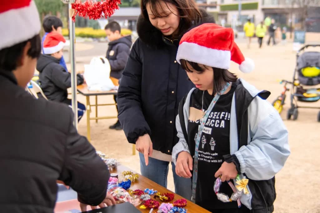 サンタ帽の子どもが、手作りのリースを並べた屋台で店番をしている