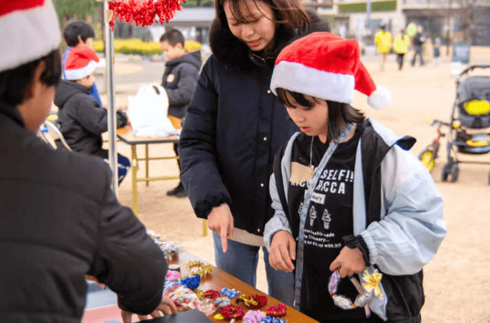 クリスマスマーケットの屋台で、子どもが手作りの品を並べている